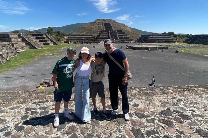 Un groupe de personnes se tient devant des ruines antiques, avec des pyramides à degrés en arrière-plan. 2