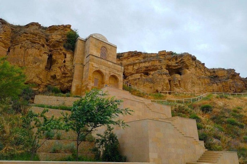 A stone staircase leading up to a building with a dome and arched windows, set against a rocky cliff. 1