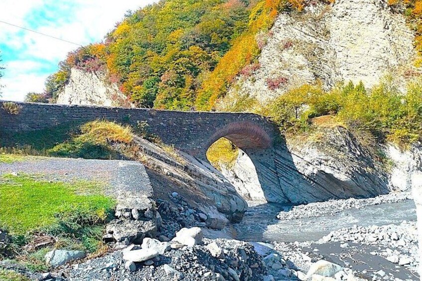 A stone bridge over a river with rocky terrain and autumn foliage. 4