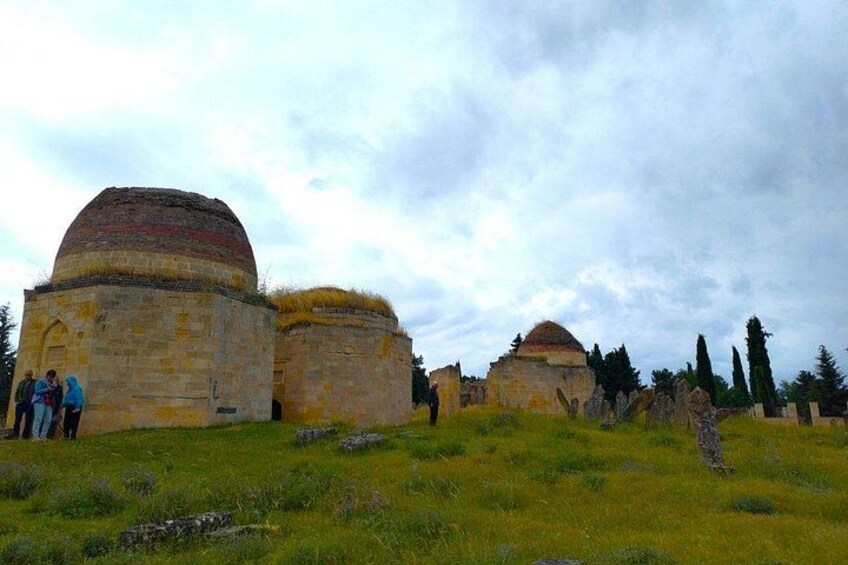 Ancient stone structures with domed roofs, a grassy field, and a cloudy sky. 3