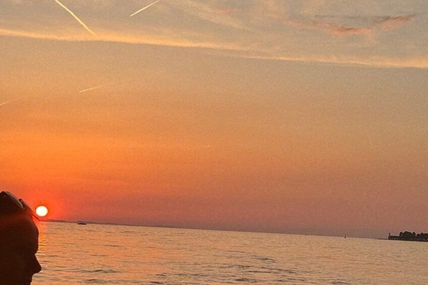 A sunset over a body of water with a silhouette of a person and a distant landmass. 4