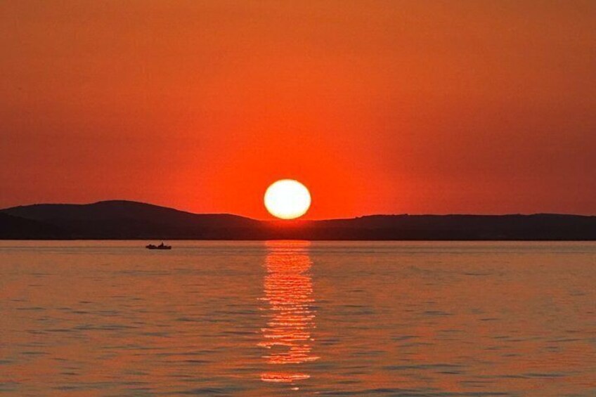 A sunset over a calm body of water with a boat in the distance and a silhouette of hills in the background. 5