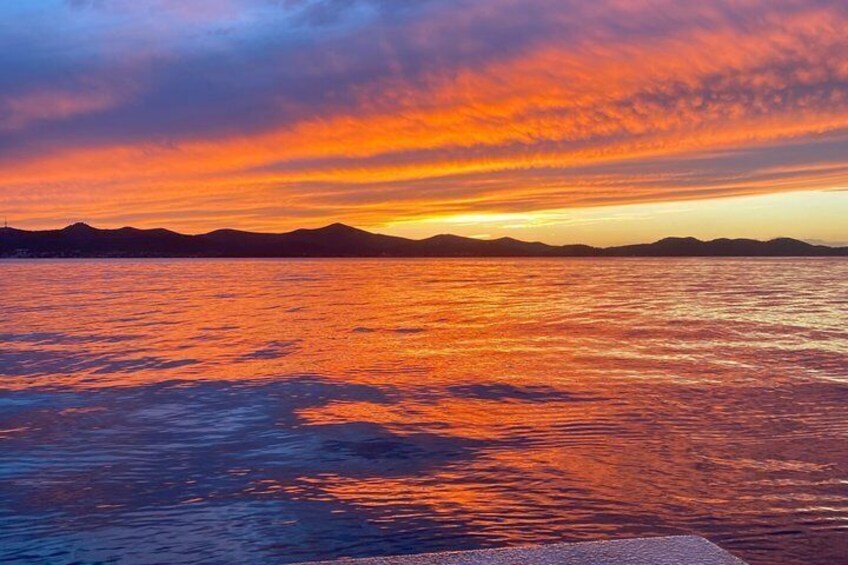 A sunset over a body of water with mountains in the distance. 1