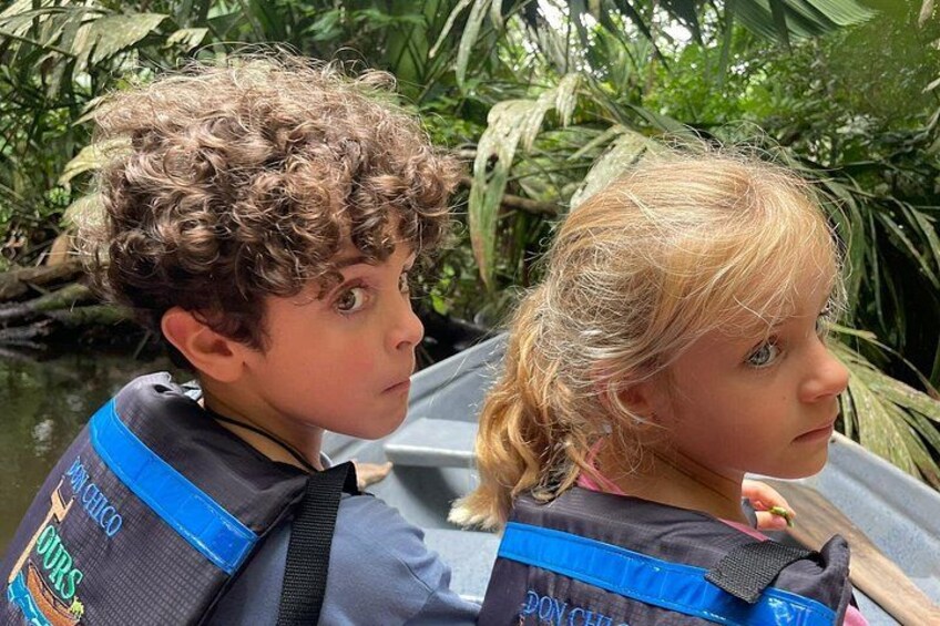 Due bambini con salvagente su una barca, immersi nel verde. 3
