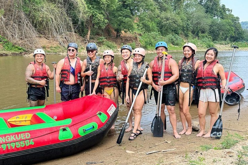 A group of people standing by a river with a red inflatable raft and paddles. 2