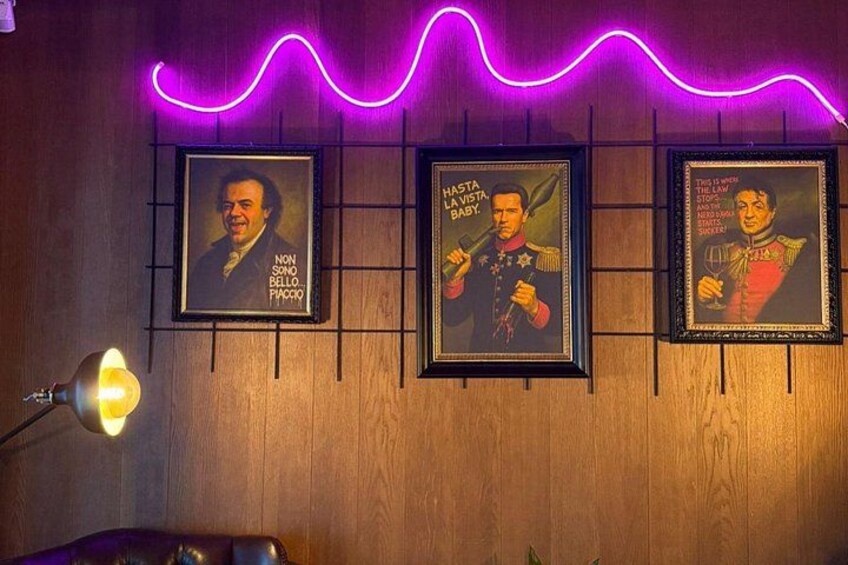 Three framed posters on a wooden wall with a neon light above. 5