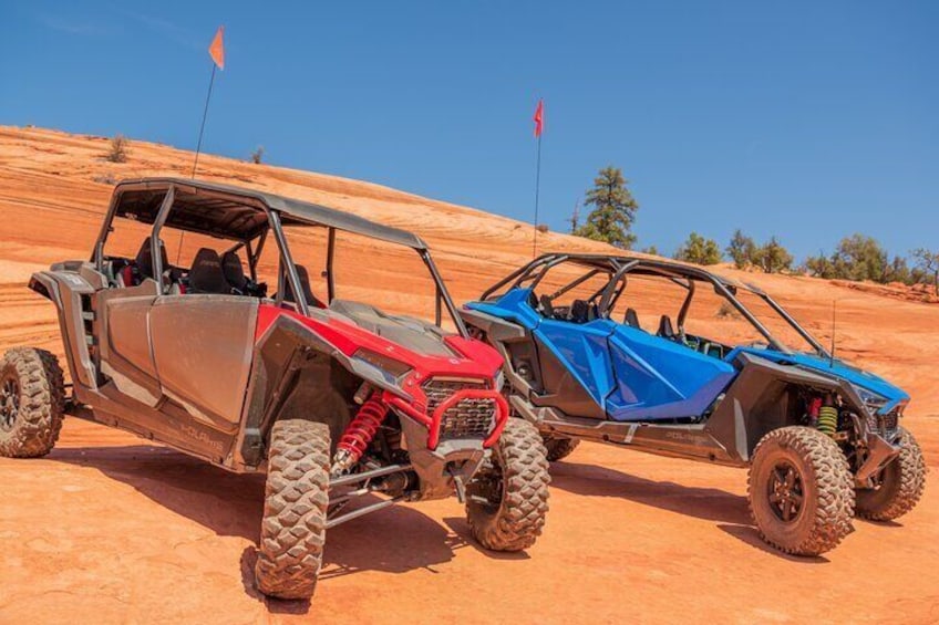 Two off-road vehicles on a desert terrain with red flags in the background. 4