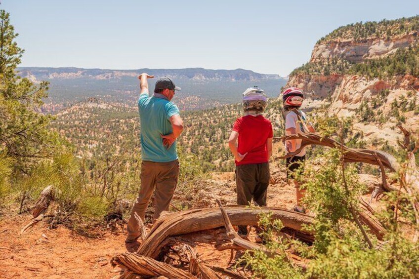 Two people hiking on a trail with a view of a valley and mountains in the background. 3