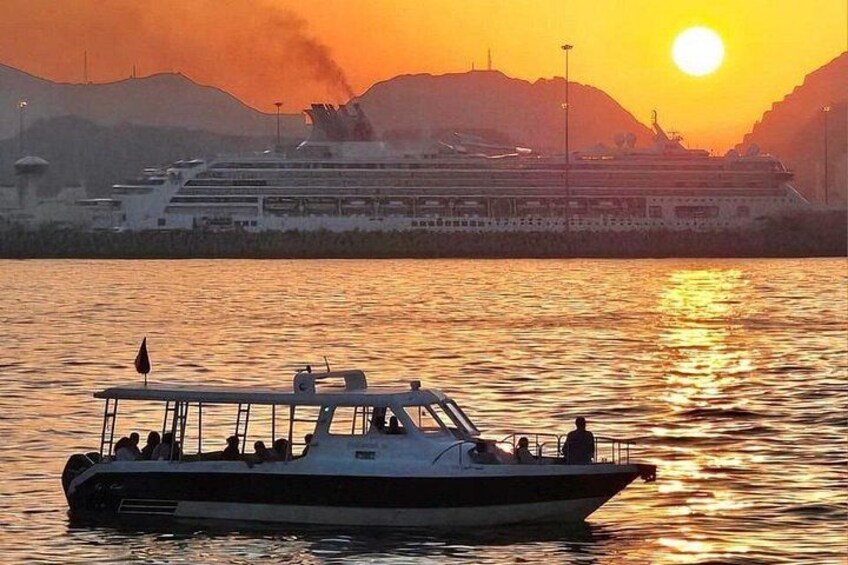 Un barco en aguas tranquilas, con un gran crucero al fondo durante el atardecer. 1