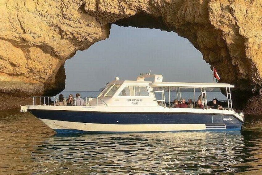 Un bote llamado 'TOURING TOURS' con pasajeros, navegando por un arco natural de roca. 2