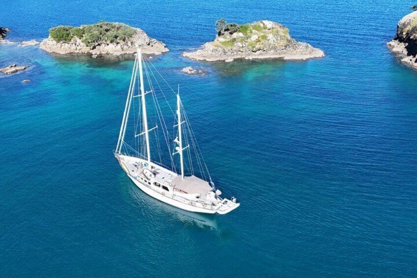 Un voilier sur des eaux d’un bleu limpide, avec des îles rocheuses en arrière-plan. 2