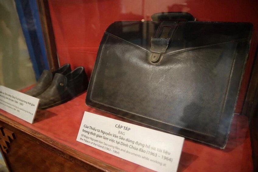 A display case with a black briefcase and a pair of black shoes. There are labels with text in Vietnamese. 4