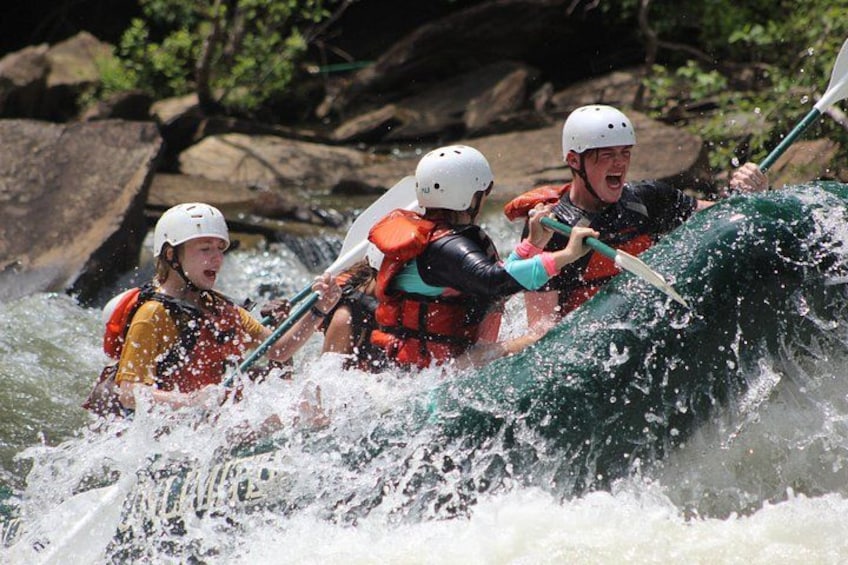 Three people in a white helmet and orange life jacket navigating a white water raft. 2