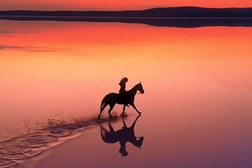 A silhouette of a person riding a horse on a reflective water surface during sunset. 3