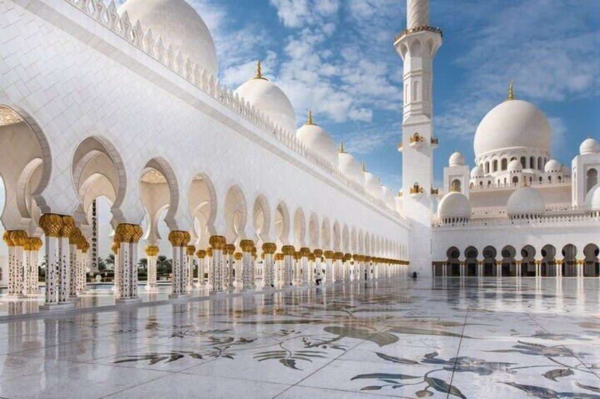 A mosque with white domes and arches, a tall minaret, and a tiled floor. 1