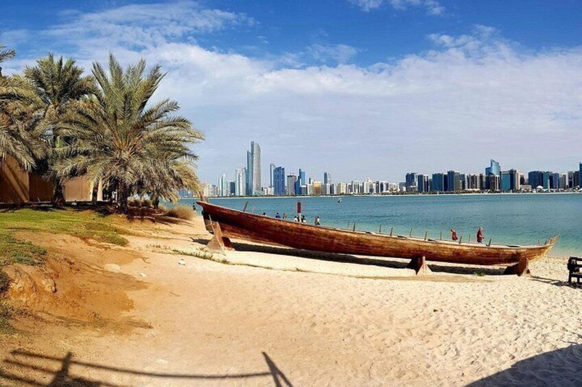 A beach with a wooden boat, palm trees, and a city skyline in the background. 4