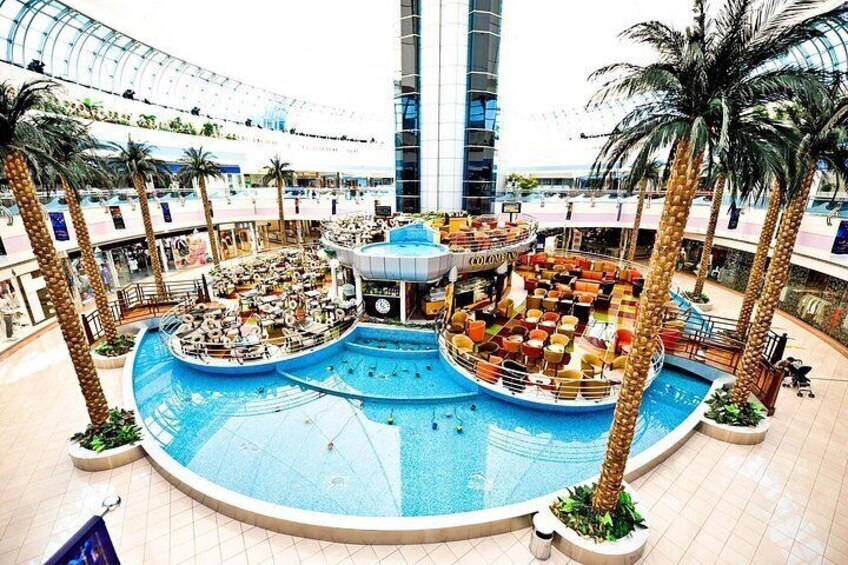 A large indoor pool with multiple seating areas, surrounded by palm trees and a high ceiling. 3
