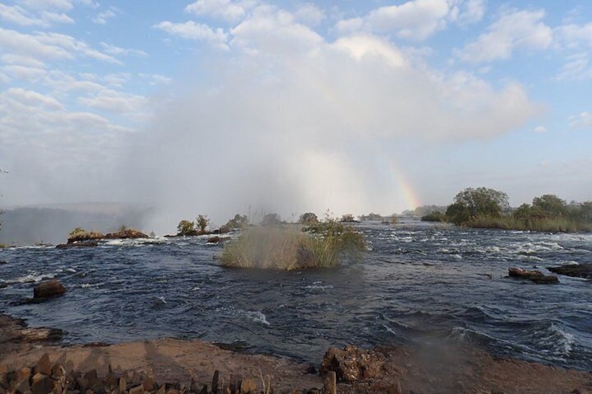 A river with a rainbow, rocks, and vegetation. 2