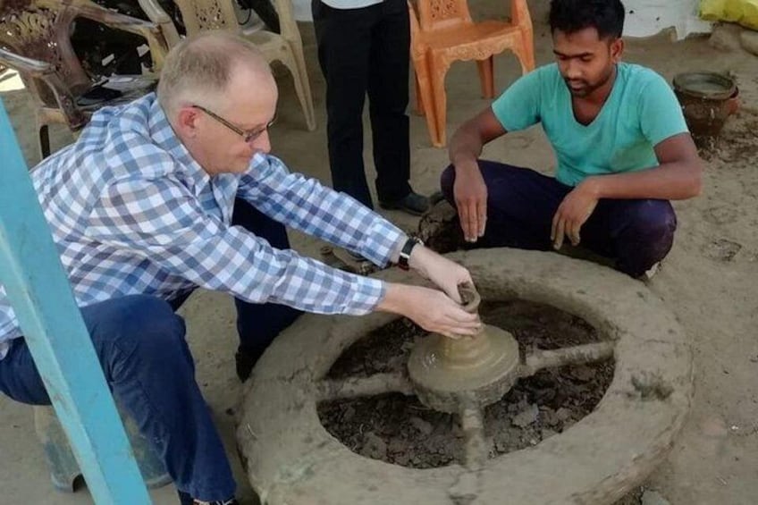 Two people working on a pottery wheel, surrounded by chairs and a rustic setting. 5