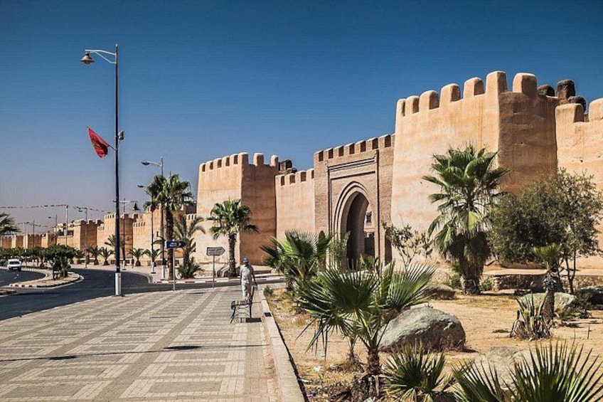 A fortified building with a large archway, palm trees, and a paved walkway. 2