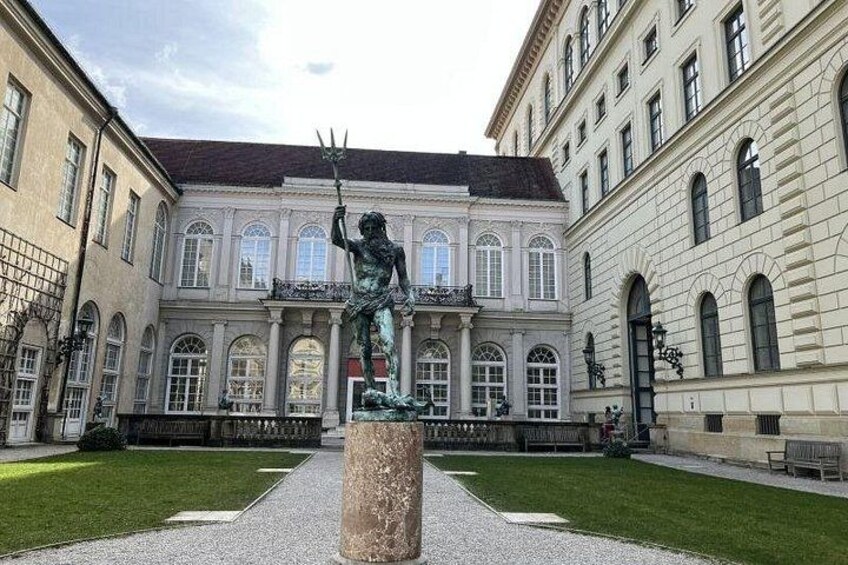 En klassisk statue i en gårdhave med en stor bygning i baggrunden. 2
