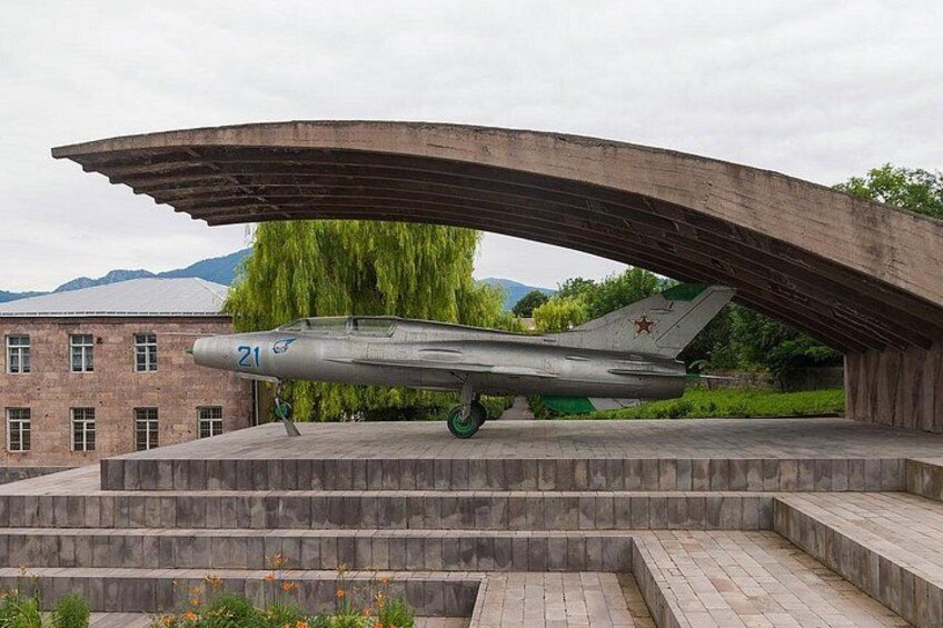 Een militair vliegtuig met het nummer 21 op de neus, tentoongesteld onder een gebogen constructie. 3