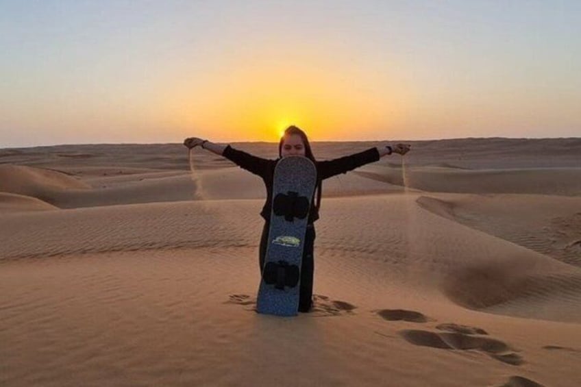 A person standing in a desert with sand dunes and the sun setting in the background. 5