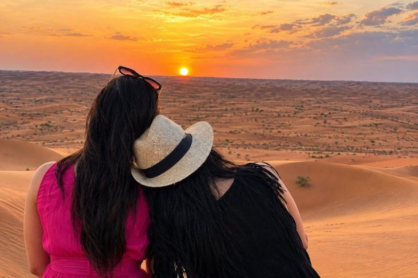 Two people standing on a sand dune with a sunset in the background. 1