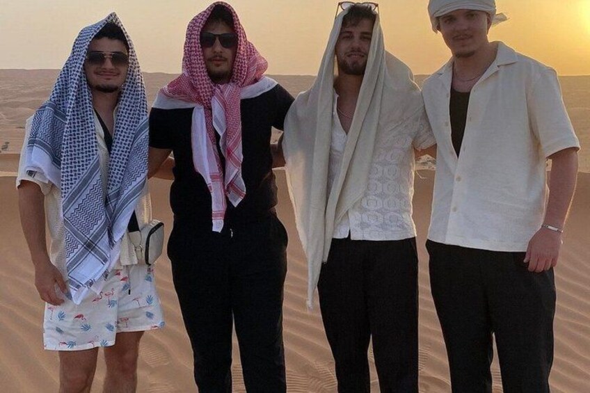 Four people standing on a sandy beach with a desert landscape in the background. 3