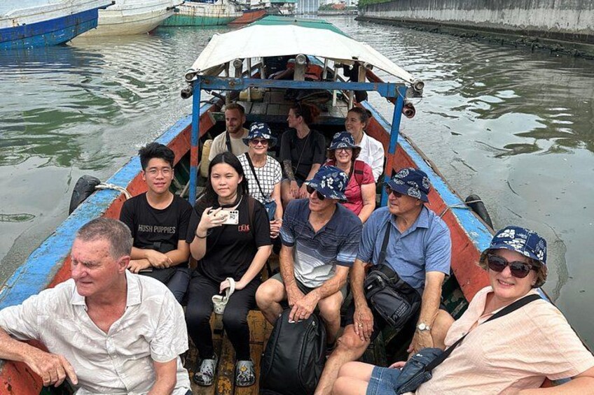 A group of people on a boat with a blue and red hull, some wearing hats, and a calm water body in the background. 3