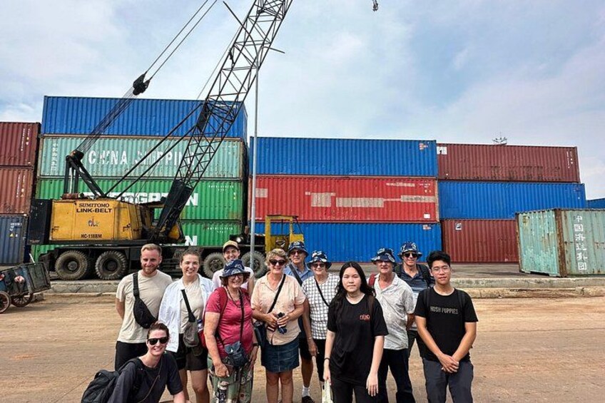 A group of people standing in front of shipping containers with a crane in the background. 4