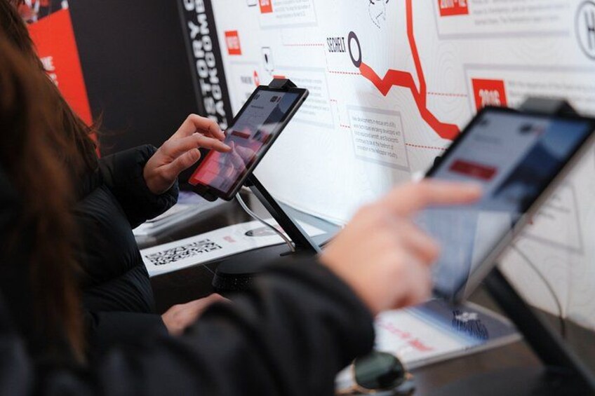 A person using a tablet and a smartphone at a booth with a QR code and a poster with text and graphics. 3