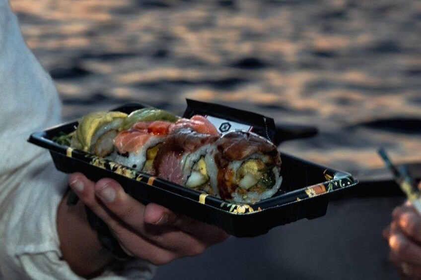 A person holding a black takeout container with sushi. 4