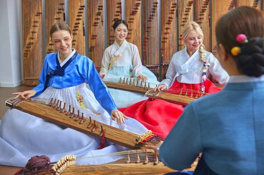 Vier mensen spelen traditionele snaarinstrumenten in een kamer met houten wandbekleding. 1