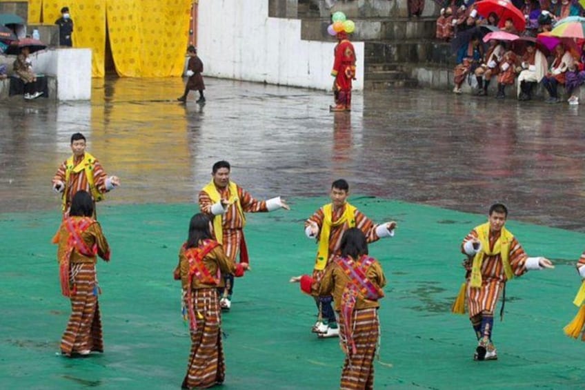 A group of people in colorful traditional attire performing a dance on a green stage. 2
