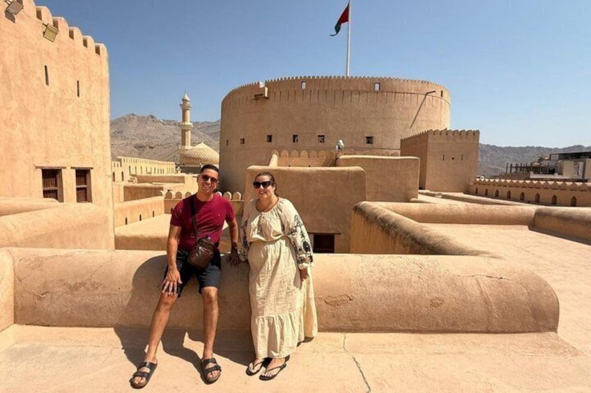 Un hombre y una mujer posan frente a una fortaleza histórica con un alminar al fondo. 1