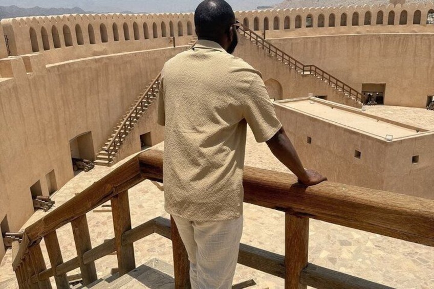 Un hombre de pie en un balcón con vistas a una fortaleza de ventanas arqueadas y una escalera. 3