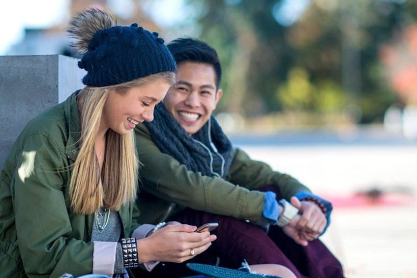 Dos personas sentadas en un banco al aire libre, una sosteniendo un teléfono inteligente. 2