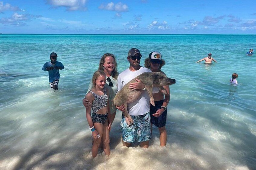 A family in shallow water with a dog, clear blue sea, and other people swimming in the background. 3