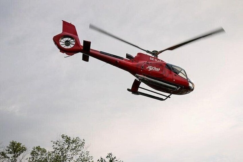 A red helicopter with 'SE-HU' and 'FlyAway' text, flying against a cloudy sky. 2