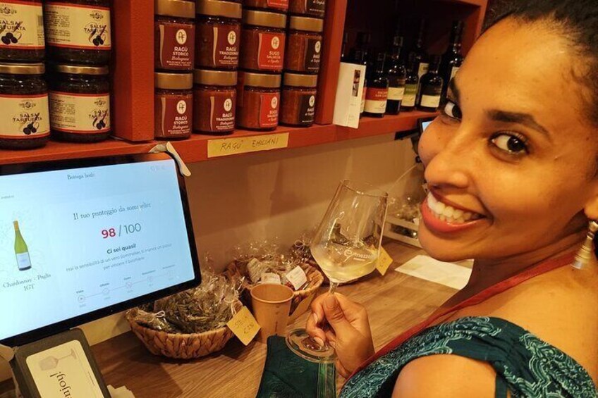 Een persoon houdt een wijnglas vast in een winkel met wijnflessen op planken en een computerscherm waarop een wijnbeoordeling staat. 4