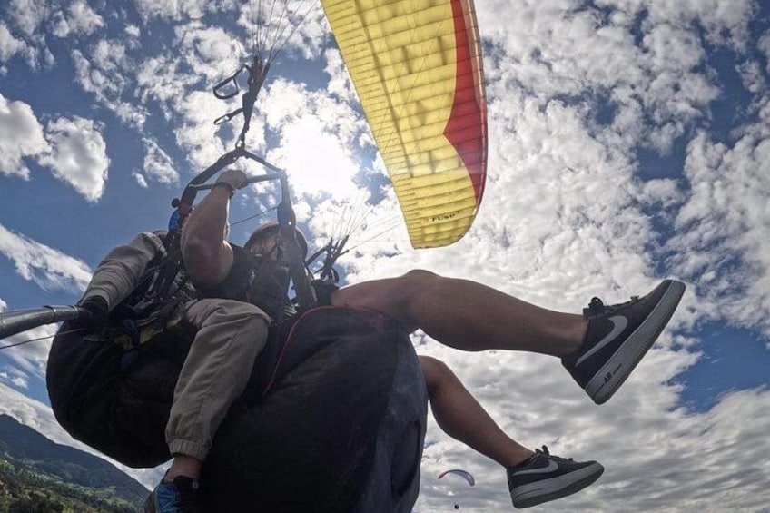 A person paragliding with a parachute, wearing a helmet, and holding onto the harness. 1