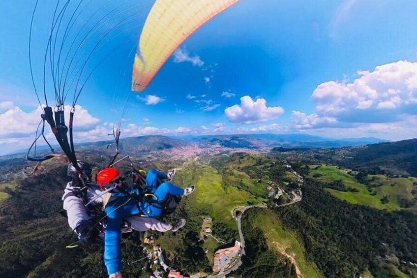 A paraglider in mid-flight over a mountainous landscape with green valleys and scattered buildings. 2