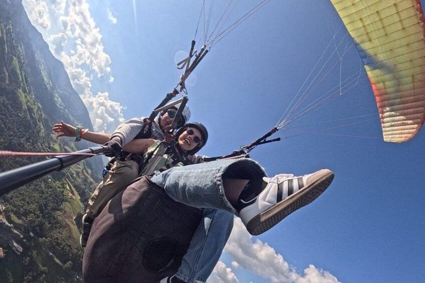 A person skydiving with a parachute, wearing a helmet and harness, and another person in the background. 5