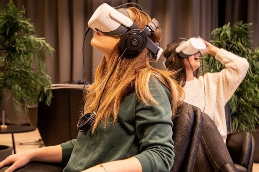 Dos personas usando cascos de realidad virtual en un espacio interior con plantas y una cortina de fondo. 2