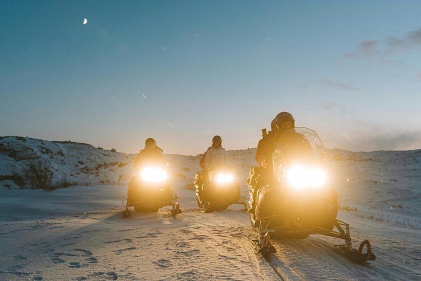 Three people on snowmobiles in a snowy landscape with a clear sky. 1