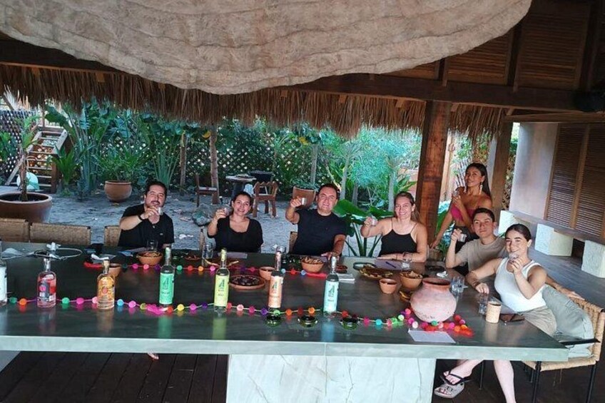 A group of people seated at an outdoor table with drinks and snacks, under a thatched roof. 5