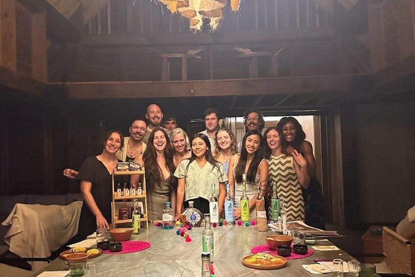 A group of people gathered around a table with bottles and glasses, in a room with wooden beams and a chandelier. 3