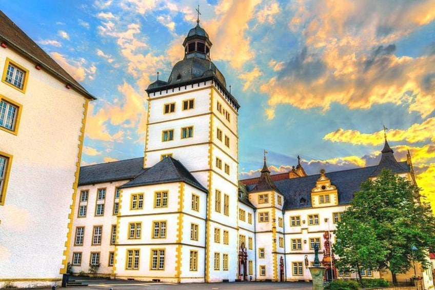 A historic building with a prominent tower and multiple windows, set against a backdrop of a clear sky with scattered clouds. 2