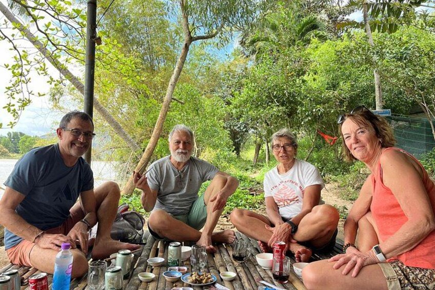 Four people sitting at a wooden table outdoors with drinks and snacks. 5